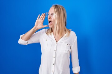 Poster - Young caucasian woman standing over blue background shouting and screaming loud to side with hand on mouth. communication concept.