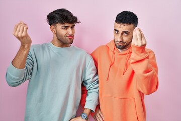Wall Mural - Young hispanic gay couple standing over pink background doing italian gesture with hand and fingers confident expression