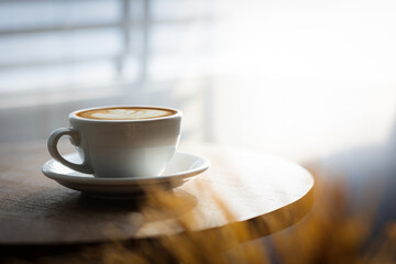 Cup of hot latte on table by white curtain window in morning