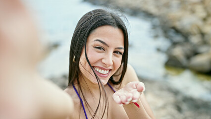 Wall Mural - Young beautiful hispanic woman tourist make selfie by camera kissing at seaside