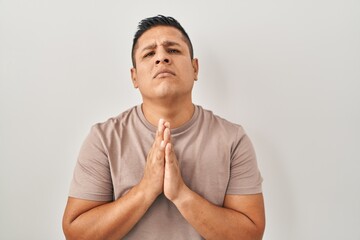 Sticker - Hispanic young man standing over white background begging and praying with hands together with hope expression on face very emotional and worried. begging.