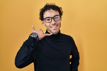 Canvas Print - Hispanic man standing over yellow background smiling doing phone gesture with hand and fingers like talking on the telephone. communicating concepts.