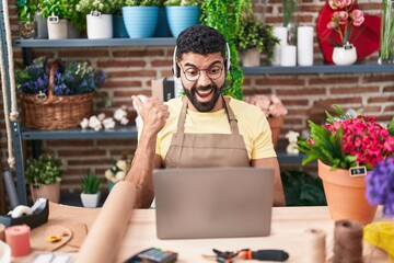 Sticker - Hispanic man with beard working at florist shop doing video call pointing thumb up to the side smiling happy with open mouth