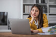 © wichayada - asian business woman thinking solving problem at work, worried serious young asian woman concerned make difficult decision lost in thought reflecting sit with laptop.