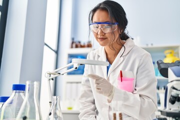 Poster - Young chinese woman wearing scientist uniform using loupe at laboratory