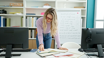 Wall Mural - Young blonde woman teacher smiling confident writing on notebook at classroom