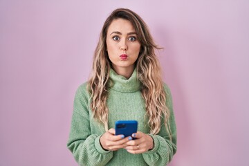 Sticker - Young caucasian woman using smartphone typing message puffing cheeks with funny face. mouth inflated with air, catching air.