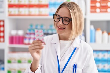 Poster - Young blonde woman pharmacist smiling confident holding pills tablet at pharmacy