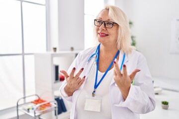 Wall Mural - Middle age blonde woman wearing doctor uniform speaking at clinic