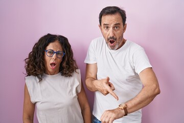 Poster - Middle age hispanic couple together over pink background in hurry pointing to watch time, impatience, upset and angry for deadline delay