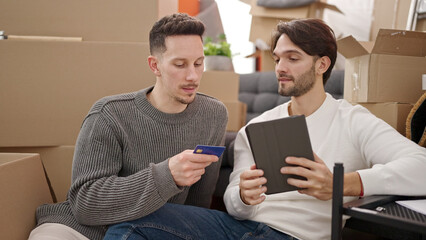 Two men couple shopping with touchpad and credit card sitting on floor at new home