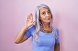 © Krakenimages.com - Middle age woman with tattoos standing over pink background waiving saying hello happy and smiling, friendly welcome gesture