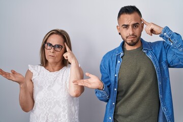 Poster - Hispanic mother and son standing together confused and annoyed with open palm showing copy space and pointing finger to forehead. think about it.