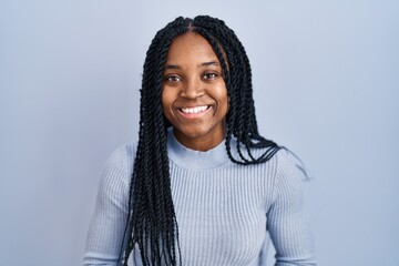 Poster - African american woman standing over blue background with hands together and crossed fingers smiling relaxed and cheerful. success and optimistic