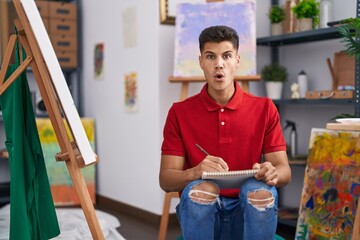 Sticker - Young hispanic man drawing on art notebook scared and amazed with open mouth for surprise, disbelief face