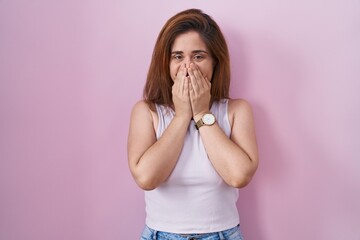 Sticker - Brunette woman standing over pink background laughing and embarrassed giggle covering mouth with hands, gossip and scandal concept