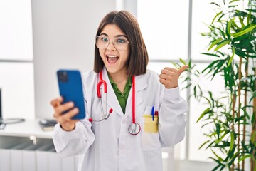 Canvas Print - Young hispanic doctor woman working on online appointment pointing thumb up to the side smiling happy with open mouth