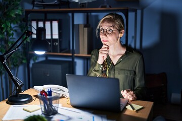 Wall Mural - Young blonde woman working at the office at night with hand on chin thinking about question, pensive expression. smiling with thoughtful face. doubt concept.