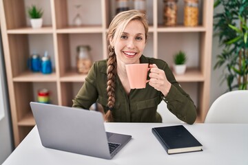 Poster - Young blonde woman using laptop drinking coffee at home