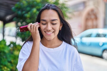 Canvas Print - Young beautiful hispanic woman miling confident listening audio message by the smartphone at street