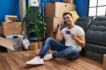 Wall Mural - Young hispanic man talking on smartphone using credit card at new home