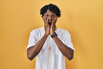 Sticker - Young african man with dreadlocks standing over yellow background afraid and shocked, surprise and amazed expression with hands on face