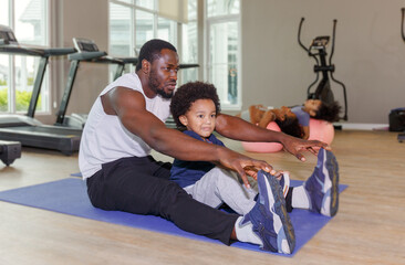 Cute boy in sportswear with smiling african american black father doing yoga on yoga mat in morning with