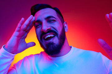 Portrait of bearded handsome man cheerfully smiling against gradient multicolored studio background in neon light. Happiness, positive vibe. Concept of human emotions, facial expression, lifestyle