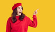 © Studio Romantic - Happy excited attractive young brunette woman in red beret and sweatshirt standing on yellow studio background, looking aside and pointing index finger at copy space side. Autumn fashion sale concept