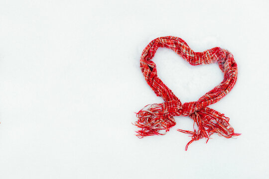 Wall Mural - red knitted scarf in the shape of a heart on white snow in winter, free space