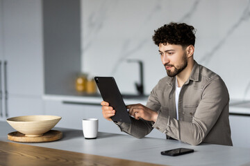 Portrait of a young man in the kitchen with a tablet at home