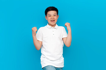 asian little boy in white t-shirt wins and celebrates victory on blue background, korean child rejoices in success