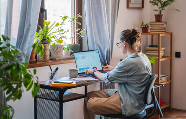 Young female freelancer working learning from home at home using laptop with chart on screen. Remote work and online education concept