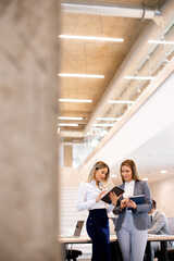 Two young business women looking at financial results on digital tablet in front of their team at the office