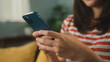 © STAGE65 - Close up of beautiful Asian woman sit on sofa hand holding mobile phone chatting with friends and playing social media. Young female looking at smartphone cellphone browsing internet at living room