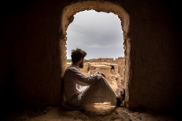 man in traditional robe sitting and looking at ancient ruins of a city at daytime