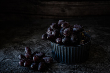 Bowl with black grapes on dark background 