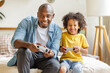 © JenkoAtaman - Happy ethnic family father and son playing video game console at home