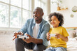 © JenkoAtaman - Happy ethnic family father and son playing video game console at home