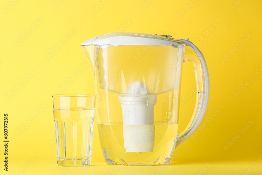 Water filter jug and glass on yellow background