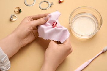 Wall Mural - Woman polishing beautiful ring with napkin on color background, closeup