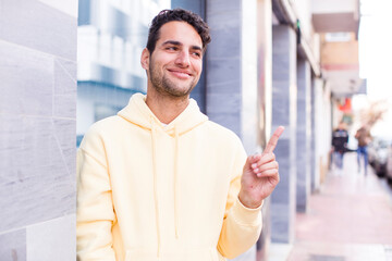 Wall Mural - young hispanic man smiling cheerfully, feeling happy and pointing to the side and upwards, showing object in copy space