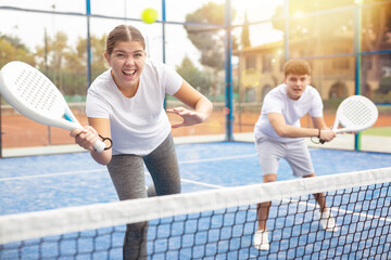 Portrait of excited male and female tennis partners playing popular sport padel game with racket outdoors