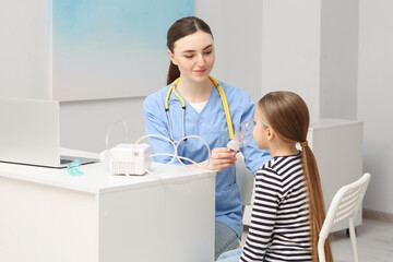 Medical assistant helping sick little girl with nebulizer inhalation in hospital