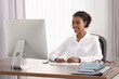 © New Africa - Smiling African American intern working with computer at table in office