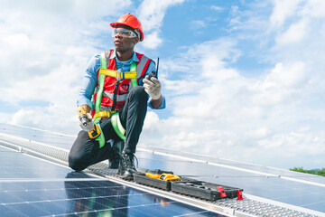 Wall Mural - African American engineer maintaining solar cell panels on factory building rooftop. Technician working outdoor on ecological solar farm construction. Renewable clean energy technology concept