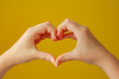 Female child hands in the form of heart isolated on yellow background