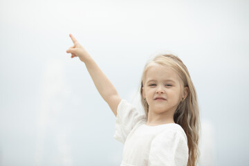 Wall Mural - Look there. Smiling little girl on the sky background pointing up with her finger. Focus at her face. Copyspace for your text or logo, banner