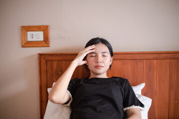 Headache woman. Close-up photo of a beautiful woman, who is sitting on a bed in bedroom with her eyes closed, touching her head while suffering from a migraine.