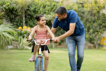 Indian father teaching riding a cycle to his daughter in lawn